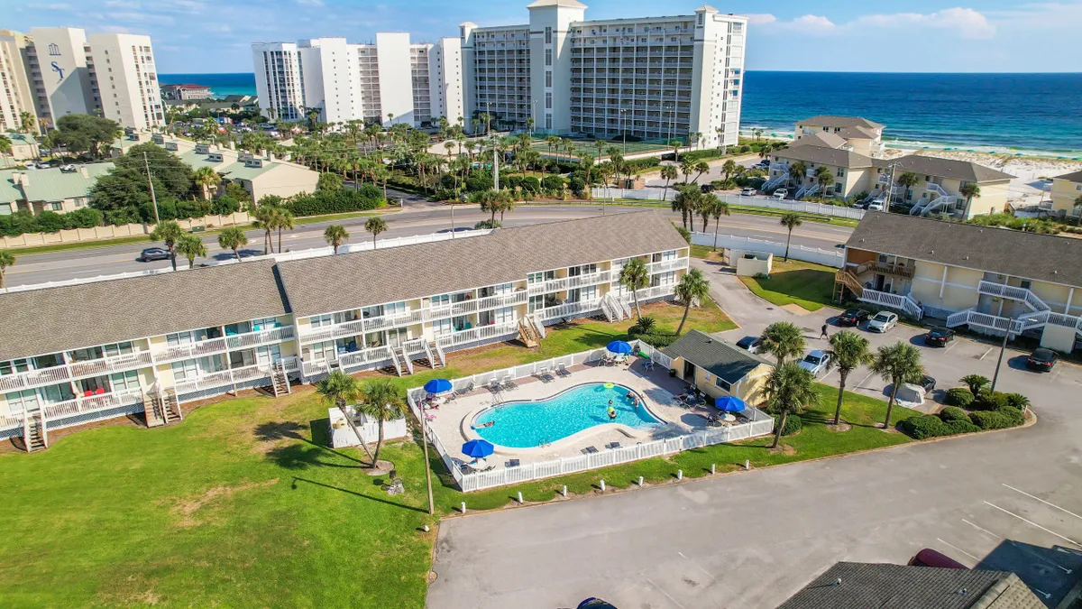 An inviting pool area surrounded by tropical landscaping, beachfront buildings, and blue umbrellas. The scene captures both the proximity to nature and the relaxed, social ambiance of the resort, with ample outdoor space and scenic views.