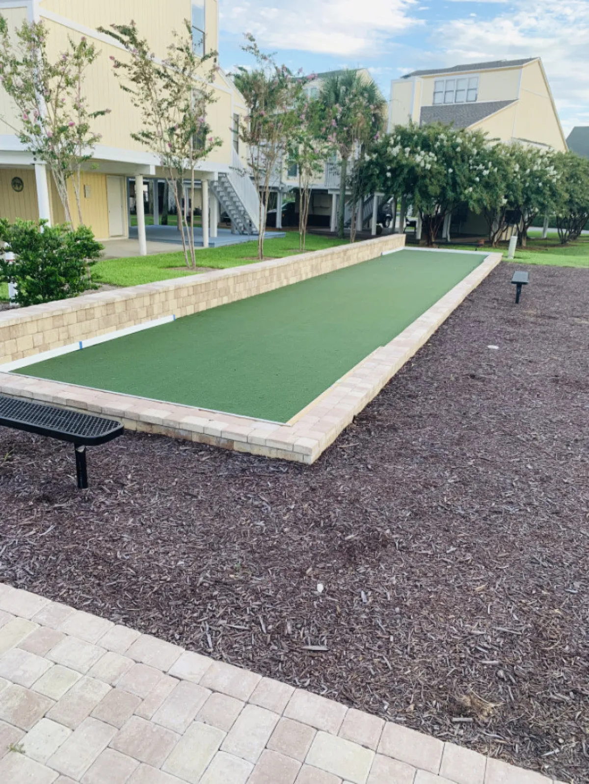 This exterior image showcases a bocce ball court set amidst landscaped areas, bordered by benches and lush greenery. The inviting scene hints at communal activities and outdoor relaxation, with open space that could be enjoyed by both residents and their pets.