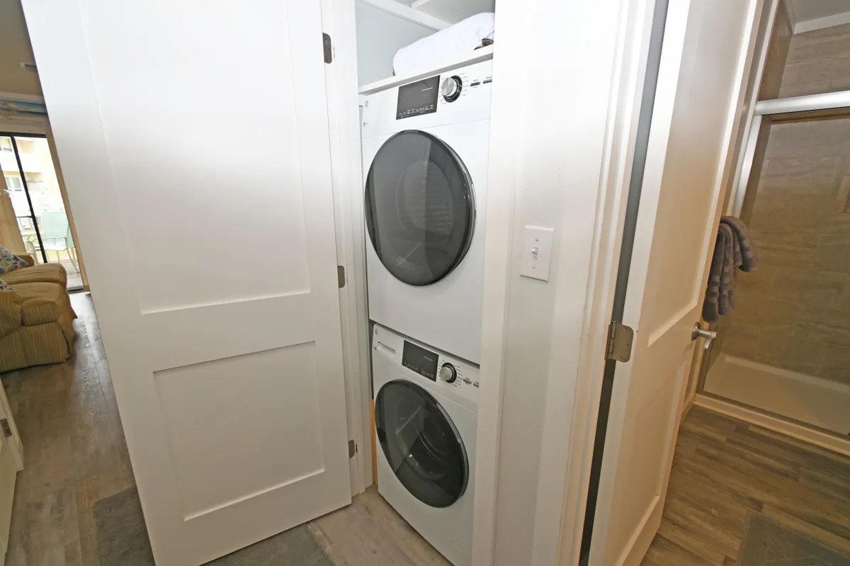 A practical, organized laundry area featuring a stacked washer and dryer set against white cabinetry, located conveniently near a bathroom door—signifying easy access and efficient use of space for everyday needs.