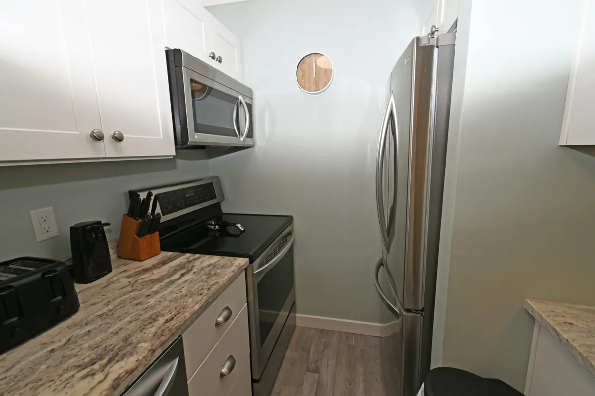 A modern, fully equipped kitchen featuring a stainless steel refrigerator with French doors, a black electric stove with oven, marble-patterned countertops, and white cabinetry with silver knobs. The space is inviting and practical, ideal for preparing fresh meals, quick snacks, or morning coffee.