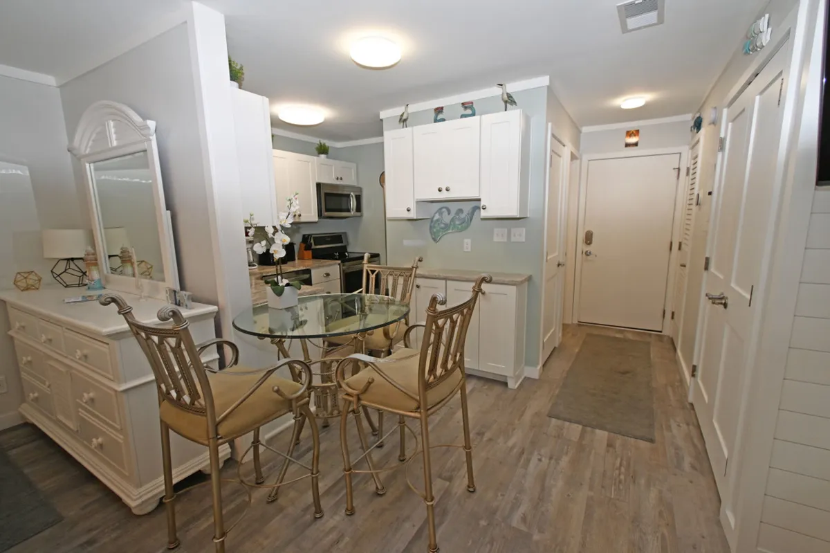 A cozy dining area with a glass-top dining table and ornate chairs, adjacent to a kitchen with modern white cabinetry and appliances. The setting is calm and comfortable, ideal for intimate breakfasts or coffee breaks, and seamlessly connects with the kitchen for easy meal transitions.