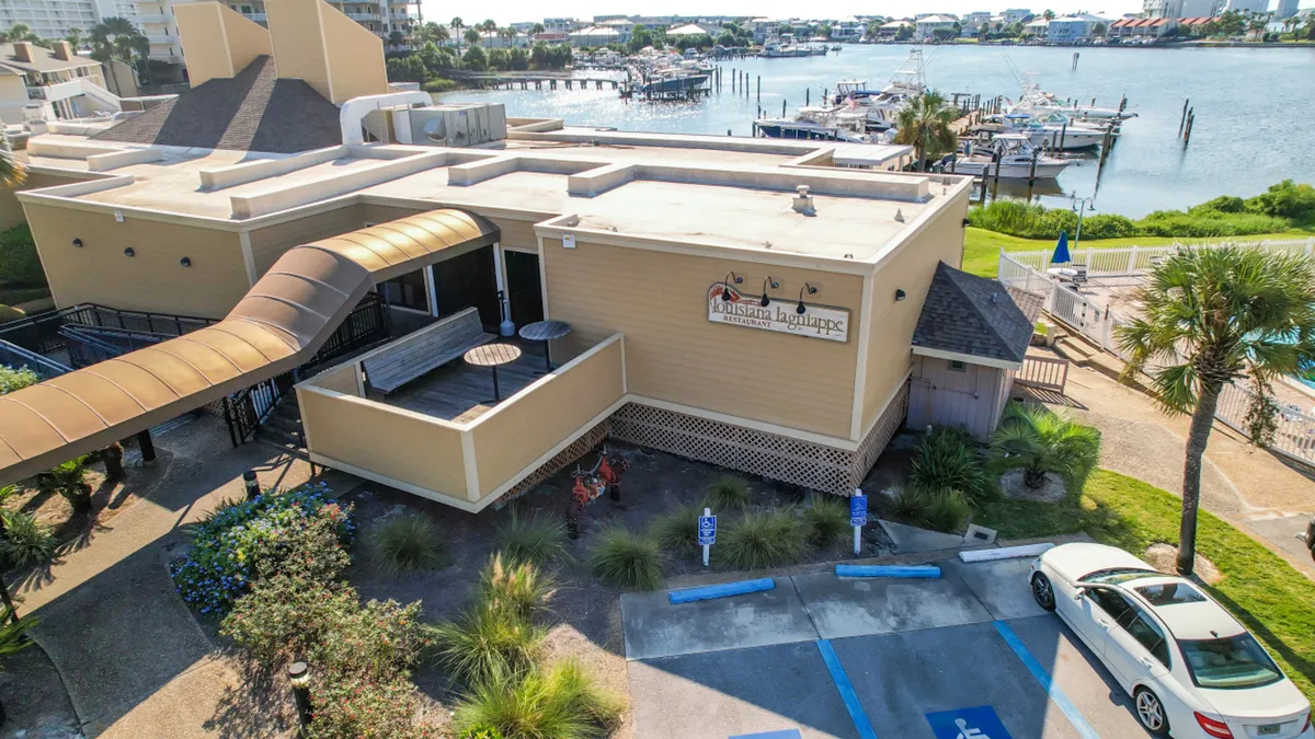 A tranquil marina scene with several docked boats, the Louisiana Lagniappe waterfront restaurant, and landscaped walkways. The area feels leisurely, inviting evening strolls or waterfront dining.