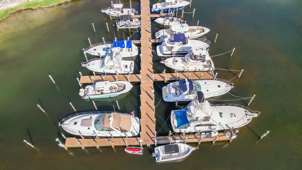 A lively marina scene with multiple boats and yachts docked along wooden piers, all surrounded by calm waters. A small red kayak is tied at the dock, hinting at a range of water sports and boating opportunities. The scene is inviting and adventurous, ideal for both relaxing and embarking on water activities.